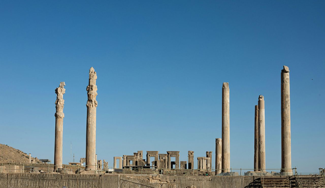 Ruins of ancient columns and stone structures at Persepolis, the ceremonial capital of the Achaemenid Empire in Iran, under a clear blue sky.