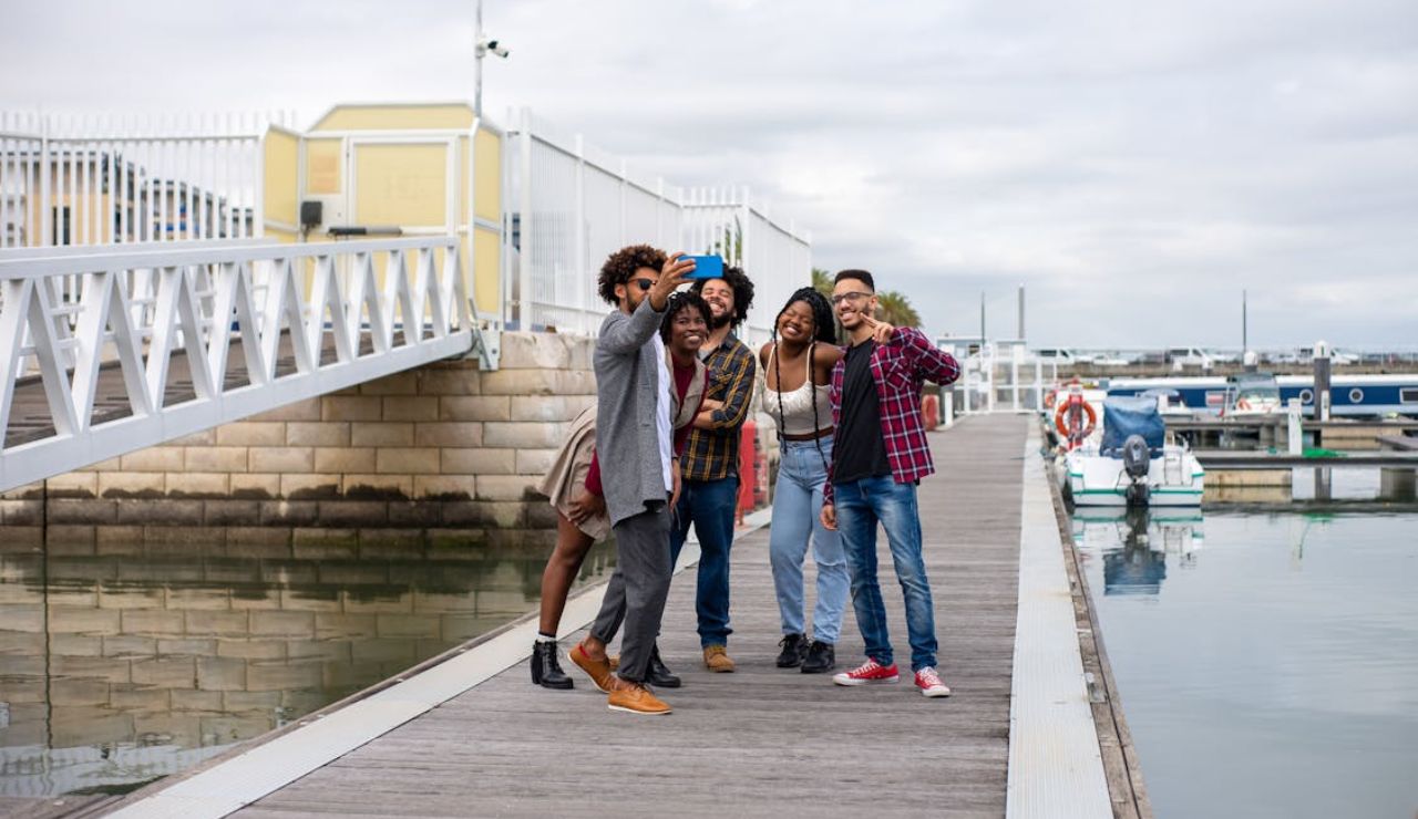 Group of friends taking a selfie on a dock near boats and water.
