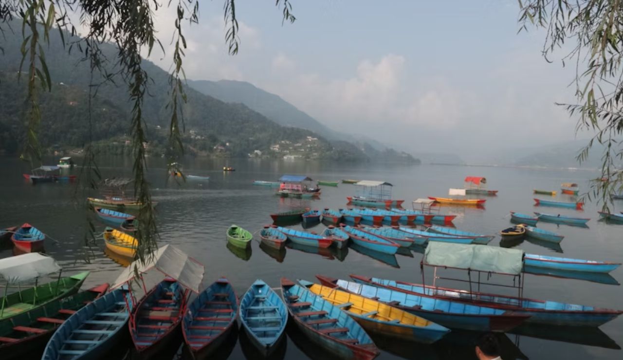 Colorful wooden boats floating on a calm lake surrounded by misty mountains and scattered clouds.