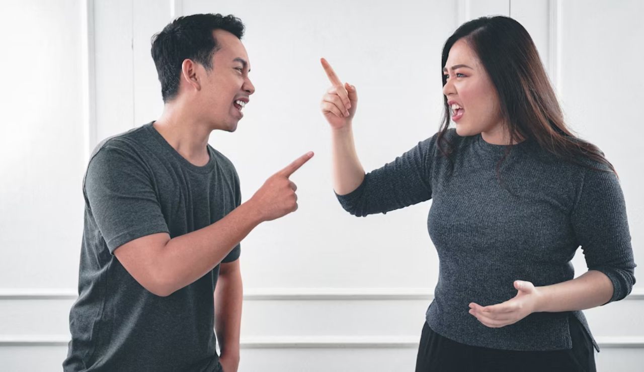 Man and woman arguing and pointing fingers at each other indoors.