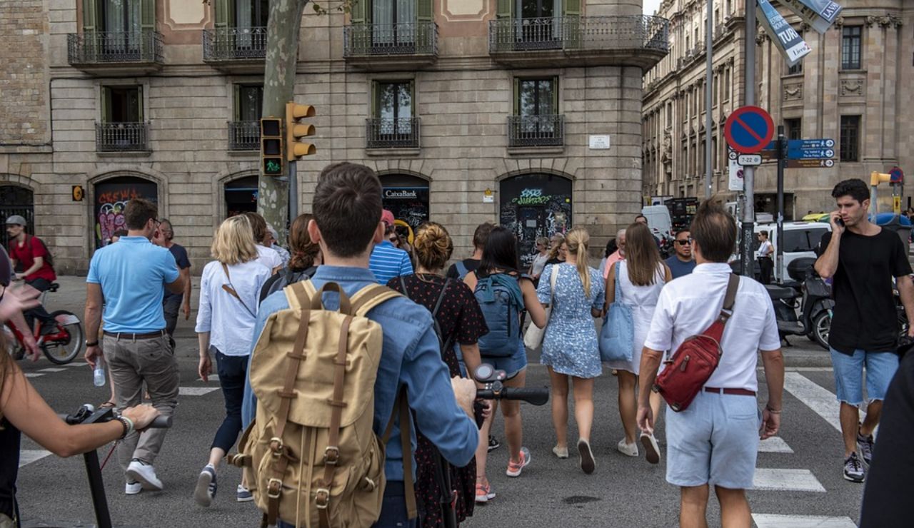 Crowd of people crossing a street in an urban European city, surrounded by historic buildings and traffic signals.