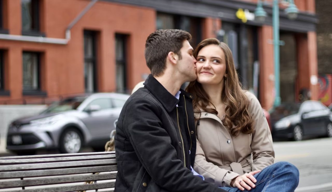 A couple sitting on a bench, sharing a tender moment, with one leaning in for a kiss.