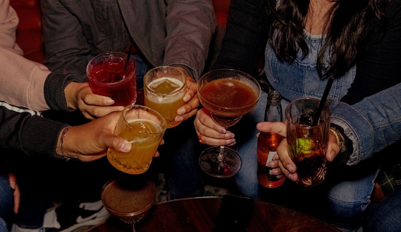 Group of friends clinking glasses with various cocktails at a bar.