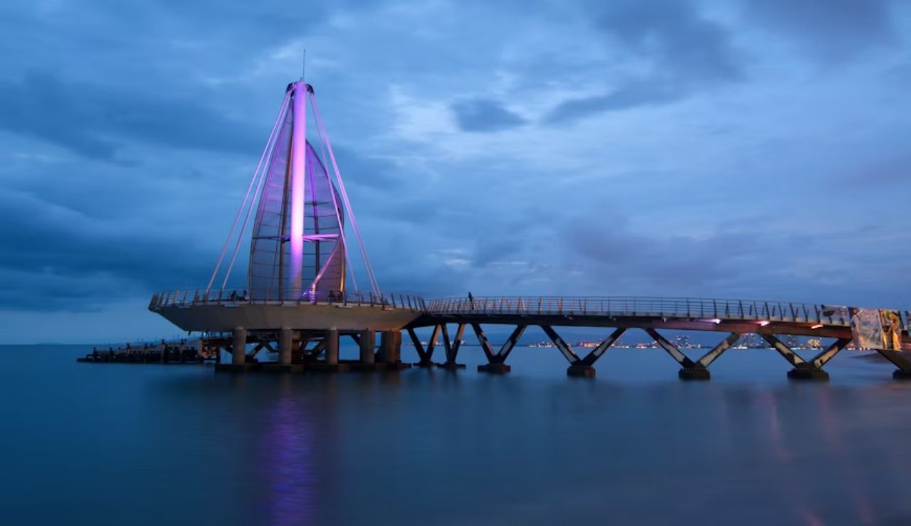 A modern pier with a glowing purple tower stretches over calm evening waters.