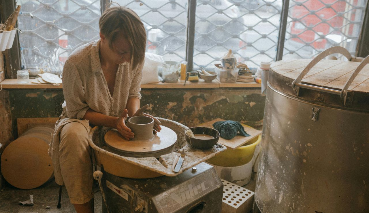 Artisan shaping pottery on a wheel in a rustic studio