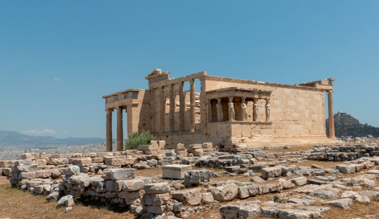 The Erechtheion temple on the Acropolis of Athens, featuring the famous Caryatid columns and surrounded by ancient stone ruins.