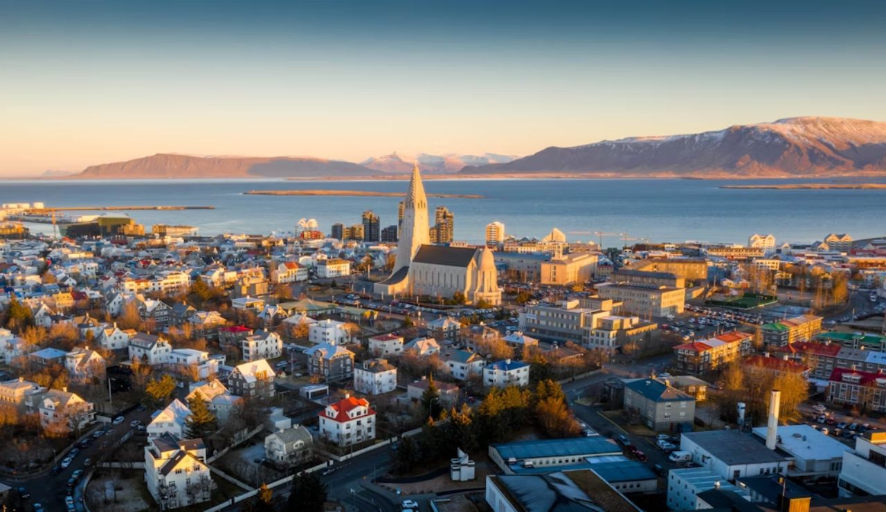 Aerial view of Reykjavik, Iceland, featuring Hallgrímskirkja church, colorful buildings, and surrounding mountains at sunset.