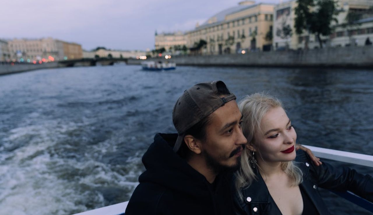 Couple enjoying a scenic river cruise with city buildings in the background.