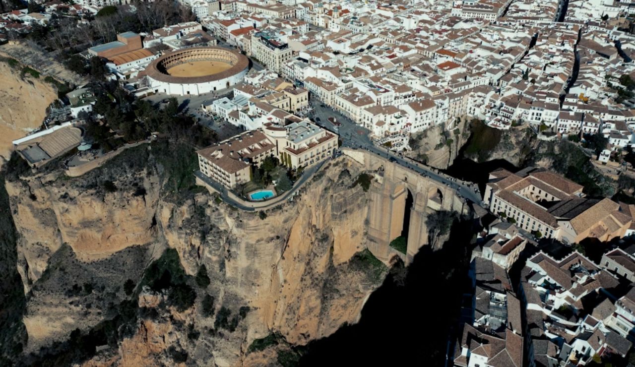 Aerial view of Ronda, Spain, featuring the Puente Nuevo bridge spanning a deep gorge and a historic bullring surrounded by whitewashed buildings.