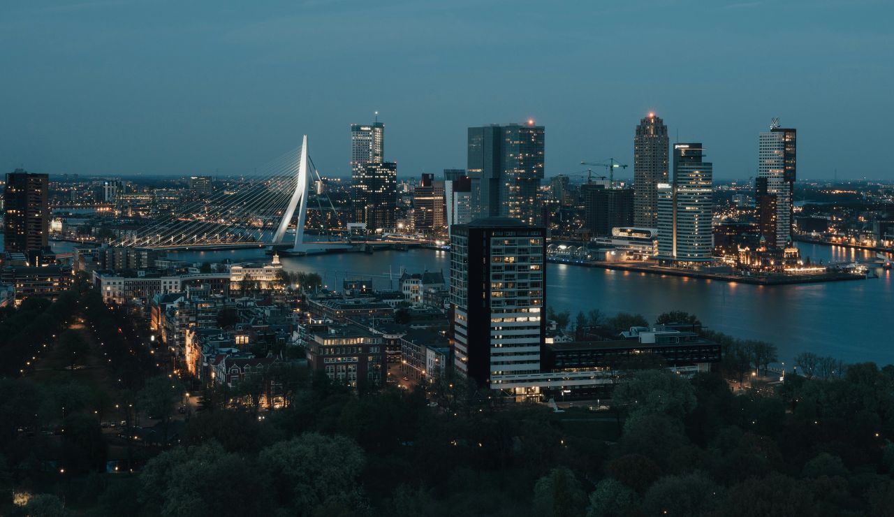 Evening cityscape of Rotterdam, Netherlands, featuring the illuminated Erasmus Bridge and modern skyline along the river.