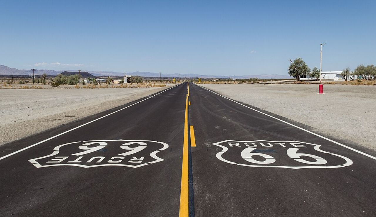 Empty stretch of Route 66 highway with painted road signs in a desert landscape.