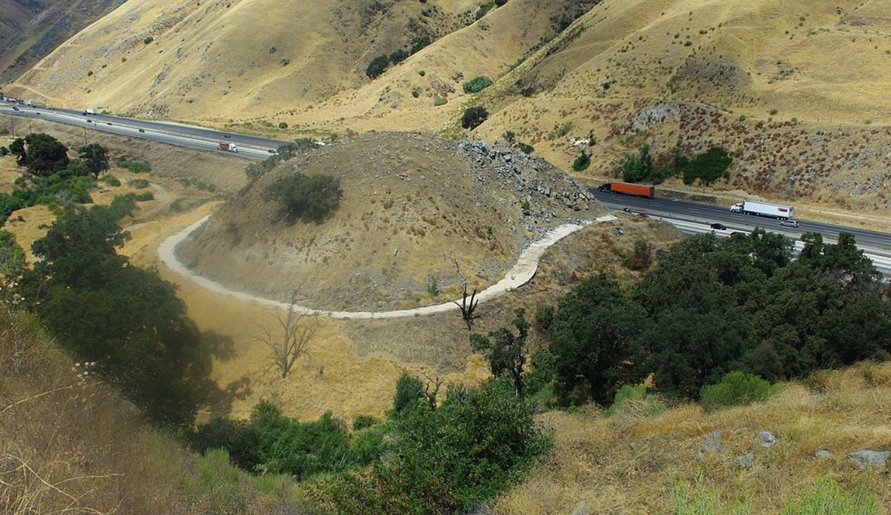 Emergency truck escape ramp winding around a hill beside a highway in dry terrain.