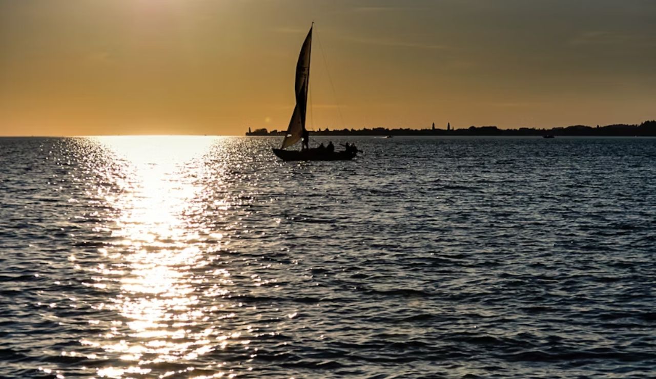 Silhouetted sailboat gliding across the sea during a golden sunset.