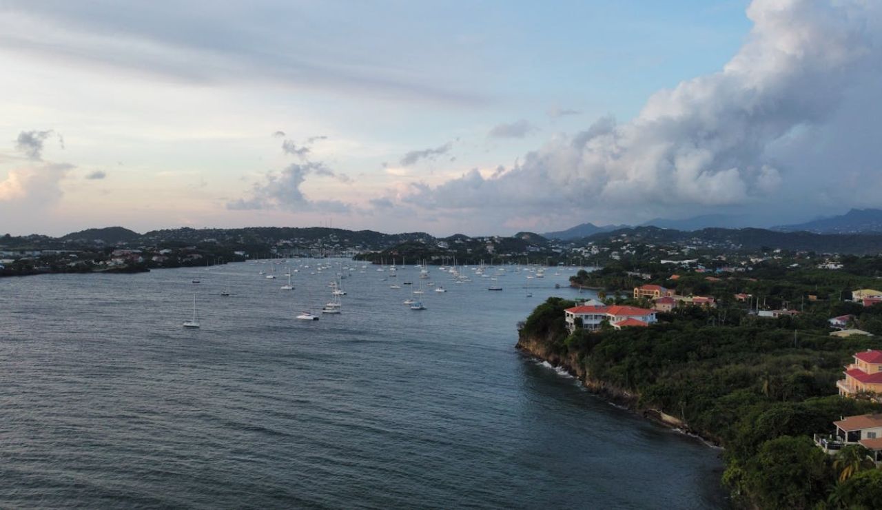 Aerial view of a coastal bay with anchored sailboats and lush green shoreline at sunset.