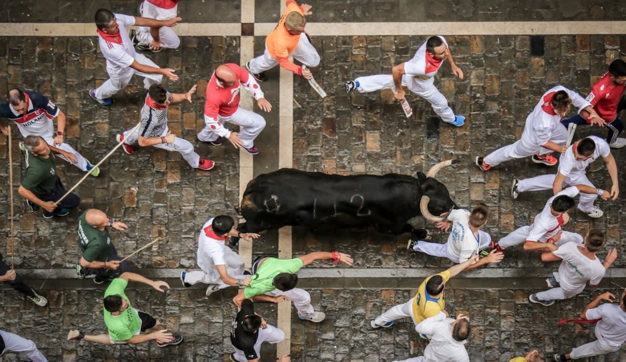 A black bull runs through a cobblestone street surrounded by people during the Running of the Bulls event.
