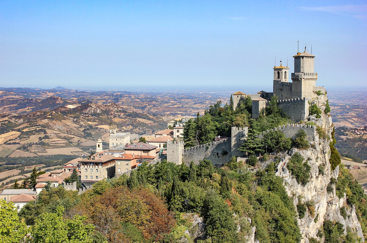 Historic fortress perched atop a rocky hill surrounded by lush greenery and a sprawling landscape under a clear sky.