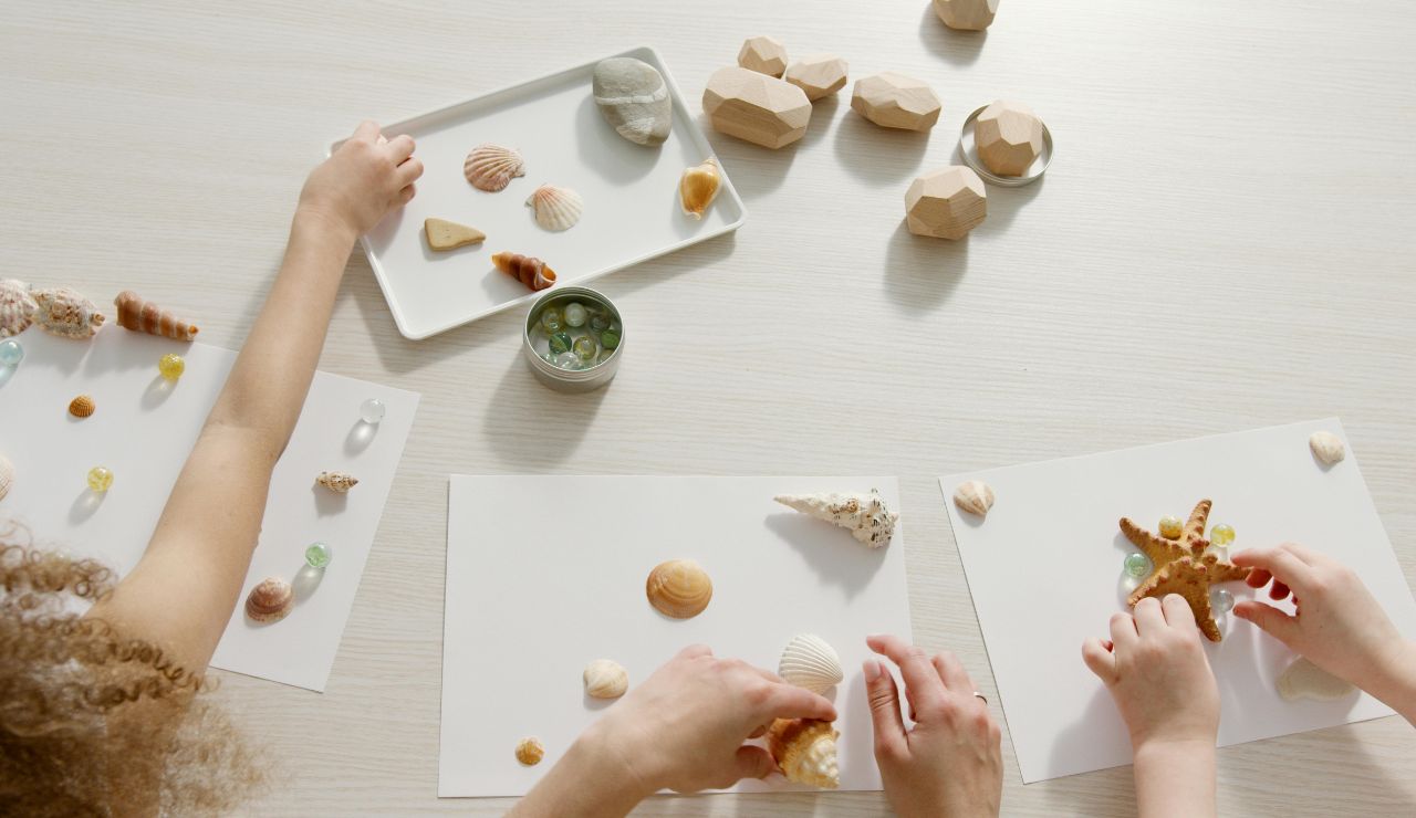 Children arranging seashells and small ocean-themed objects on paper for a creative craft activity.