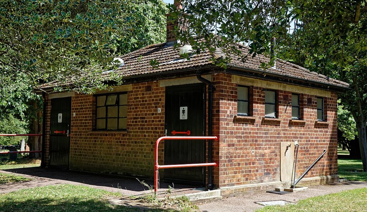 Small brick public restroom building in a park, surrounded by trees and greenery.