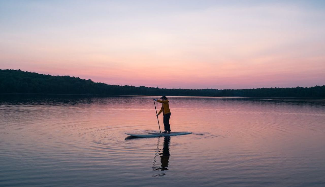A paddleboarder glides peacefully across a calm lake in Seattle at sunset.
