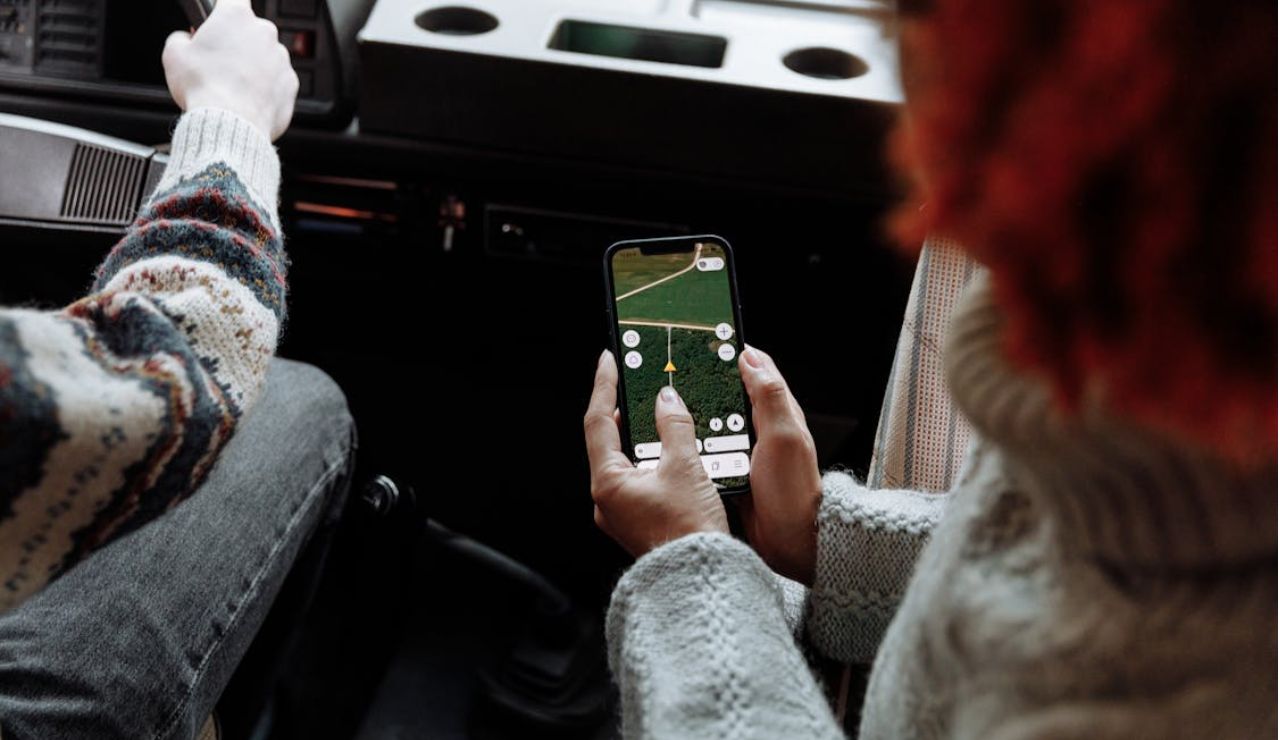 Person using a smartphone with a navigation app open while sitting in a vehicle, with another person driving.