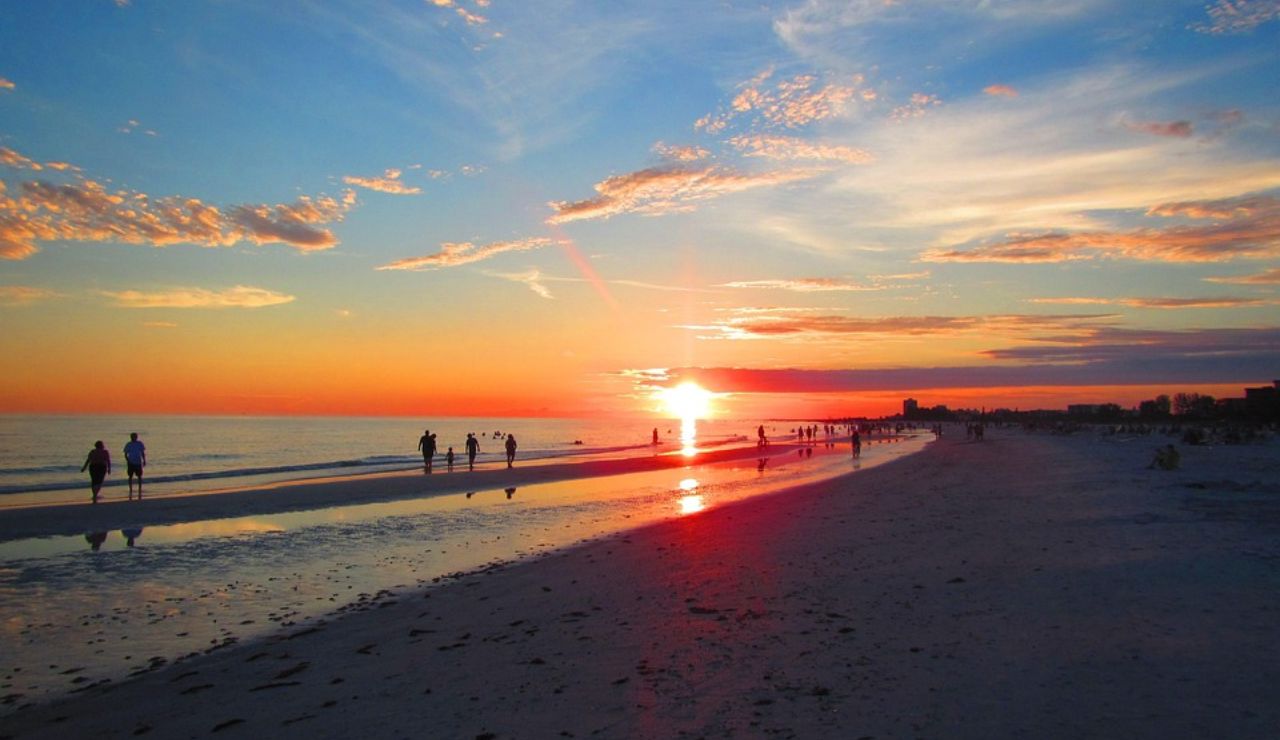 People walking along Siesta Key Beach in Florida during a vibrant sunset with colorful skies and reflections on the wet sand.