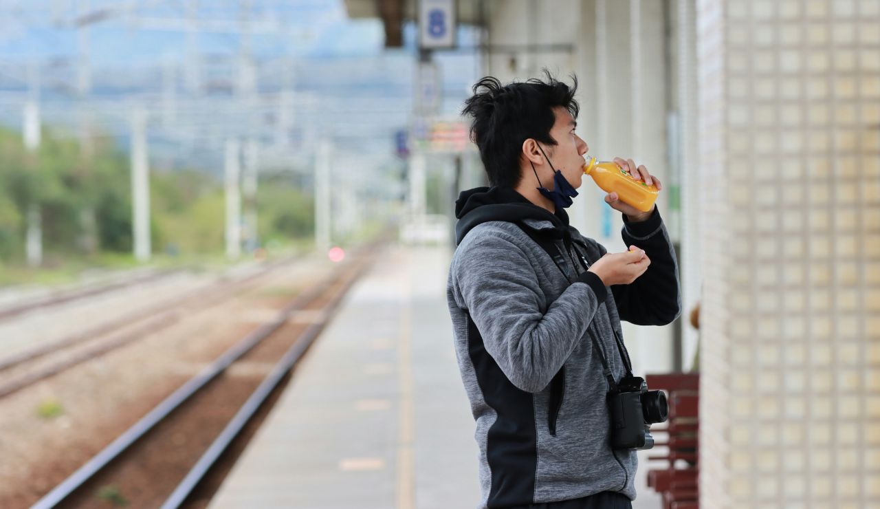 Passenger holding snacks and water at a train platform bench