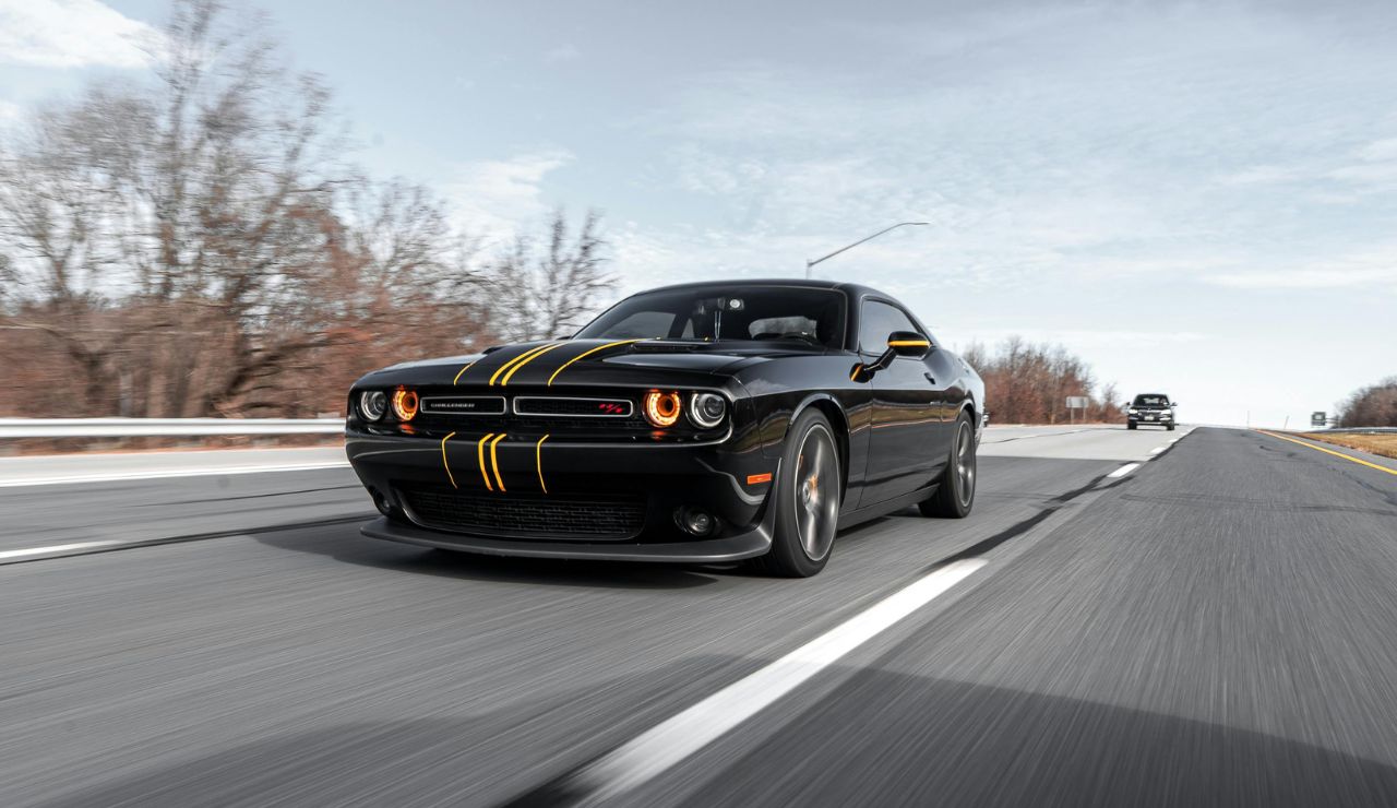 Black Dodge Challenger with yellow racing stripes driving on a highway.