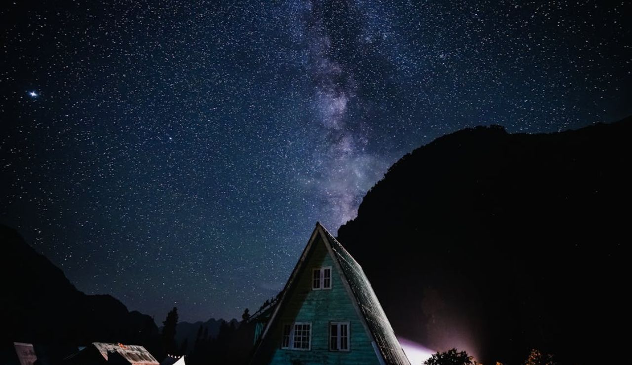 A-frame cabin under a starry sky with the Milky Way visible above.