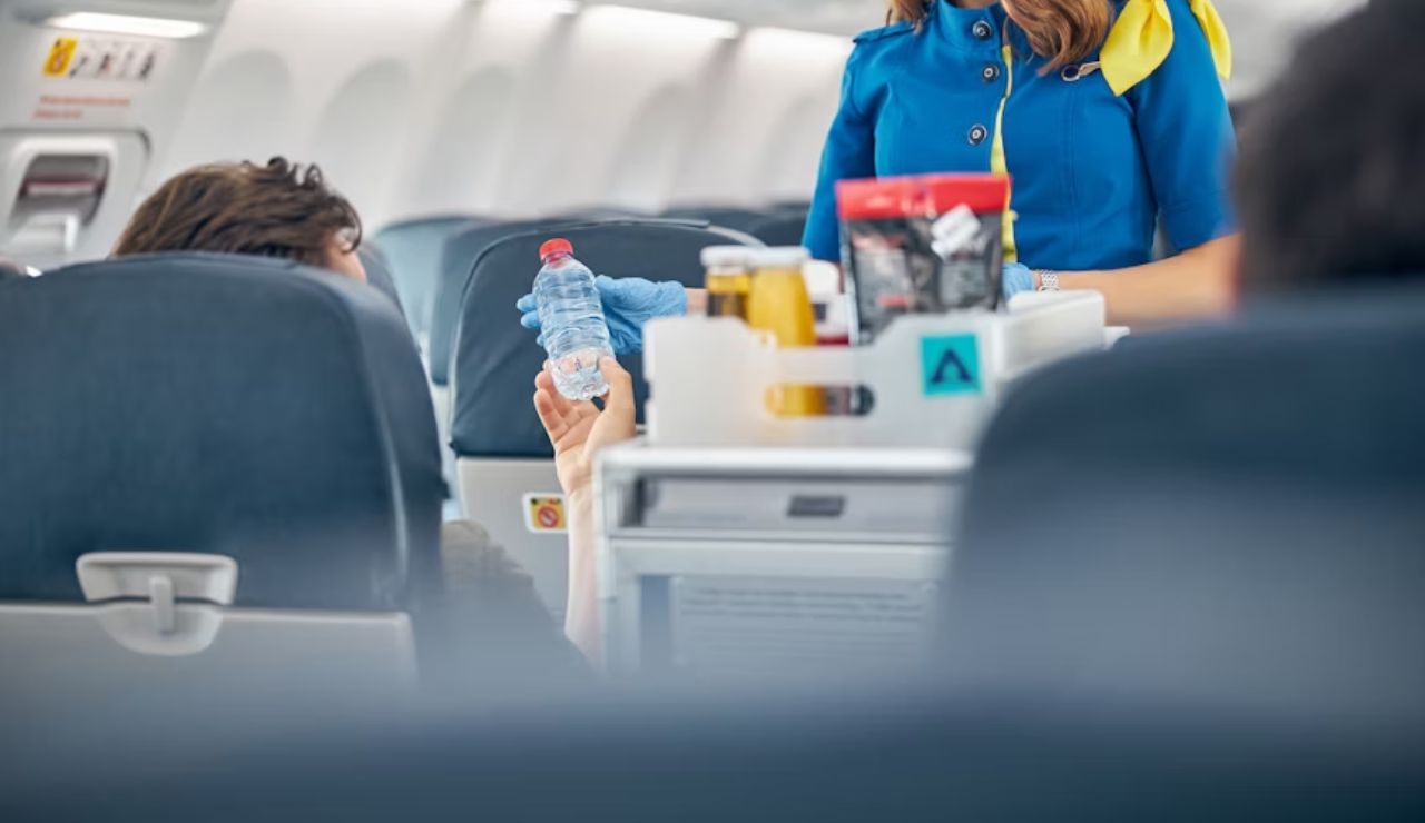 Flight attendant in blue uniform handing a water bottle to a passenger from the refreshment cart during in-flight service.