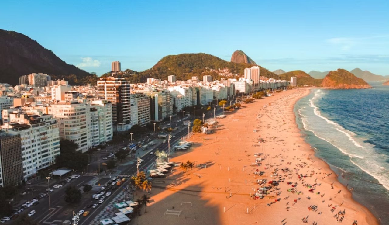 Aerial view of Rio de Janeiro's coastline with sandy beaches, vibrant city buildings, and lush mountains in the background.