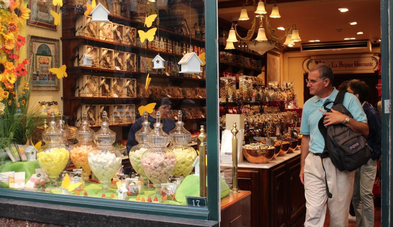 Exterior view of a colorful Belgian candy and chocolate shop with large glass jars of sweets in the window and a man entering the store.