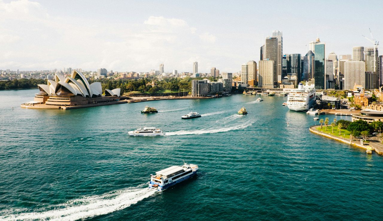 Scenic view of Sydney Harbour with boats cruising through the water, the Sydney Opera House on the left, and modern skyscrapers lining the skyline.