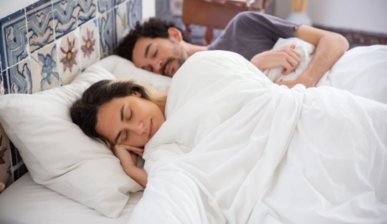 Peaceful couple sleeping together in a cozy bed with white bedding and decorative tile headboard.