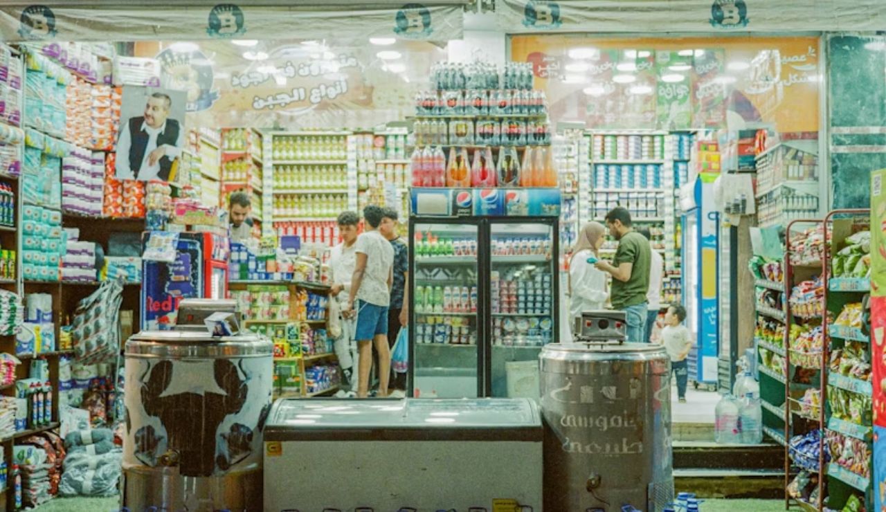Busy convenience store at night with several people shopping inside and shelves filled with drinks and packaged goods.