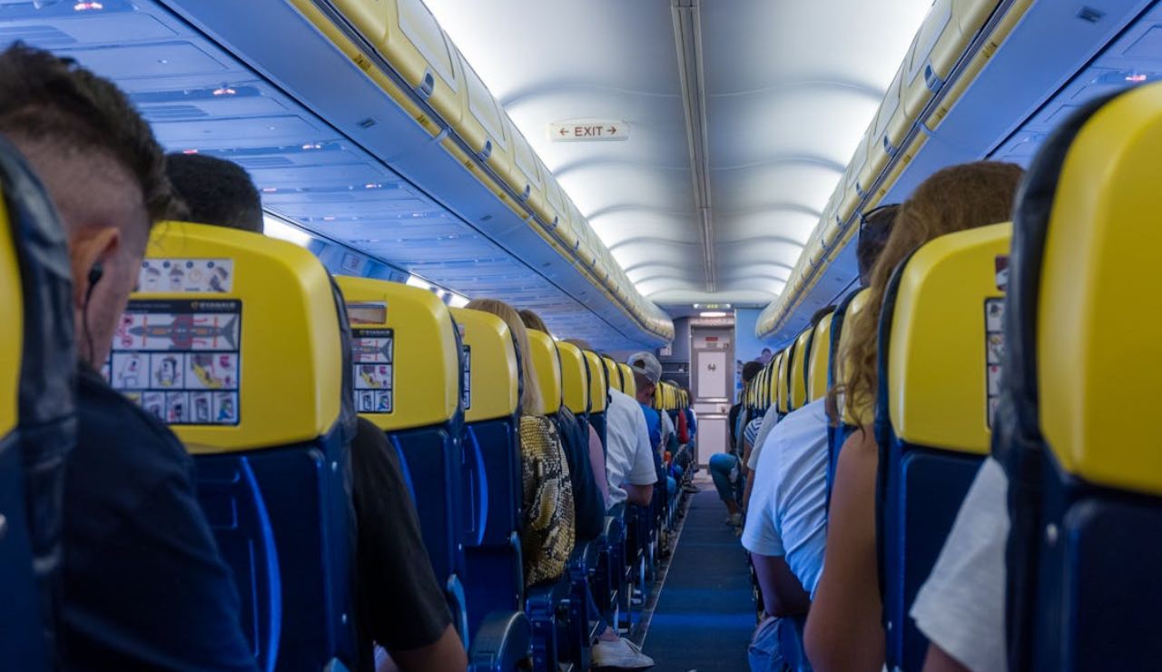 Passengers seated inside a commercial airplane with yellow and blue seats, view facing the front cabin.