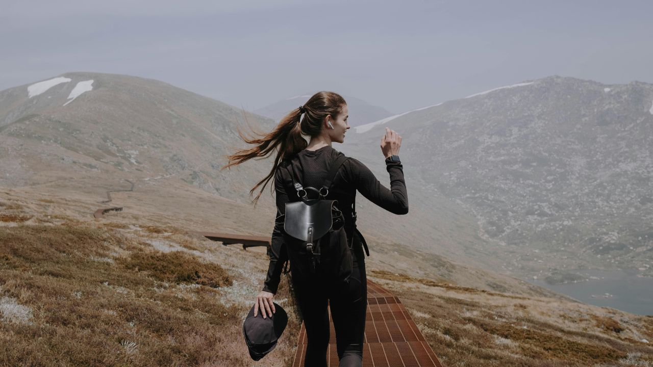 Woman in hiking gear walking along a mountain trail with scenic, misty peaks in the background.