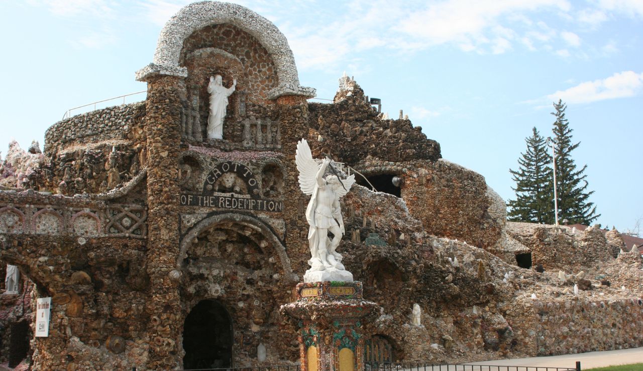 Arched stone grotto labeled "Grotto of the Redemption" features a white winged horse and rider statue at its entrance, with trees behind.
