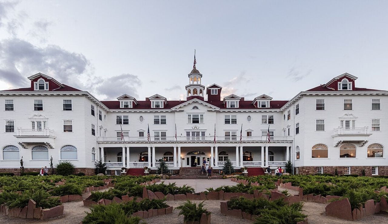 Grand historic white hotel with a red roof and central cupola, featuring a large front porch and manicured garden walkway.