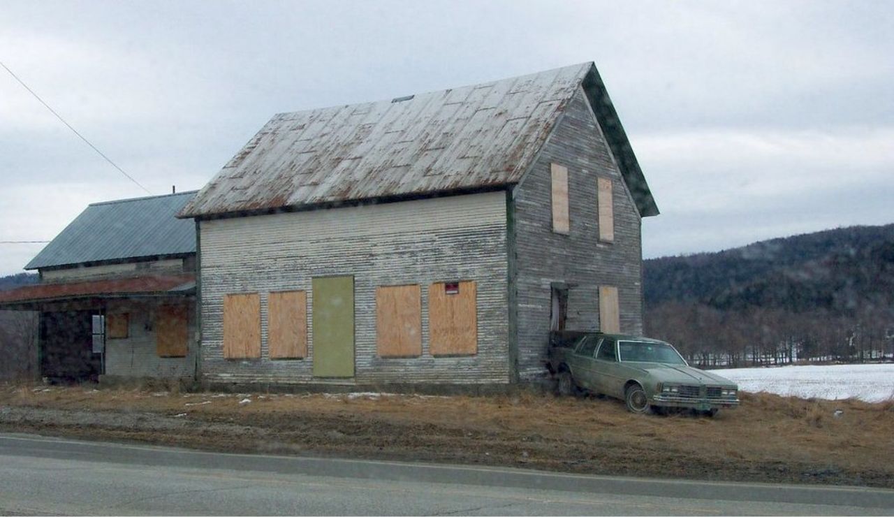 Abandoned wooden house with boarded windows and an old car crashed into it.
