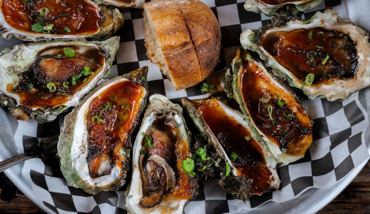 Grilled oysters topped with sauce and green onions served with bread, showcasing the thriving local food scene in the Pacific Northwest.