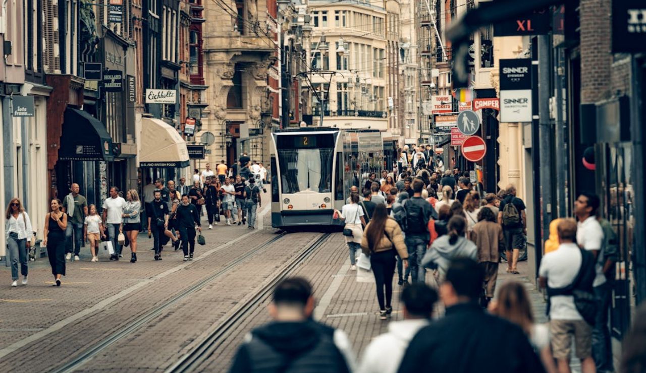 A crowded street in Amsterdam with pedestrians and a tram passing through.