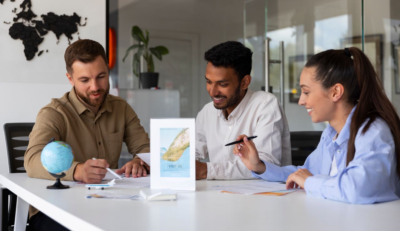 A travel agent showing cruise brochures to a couple at a desk.