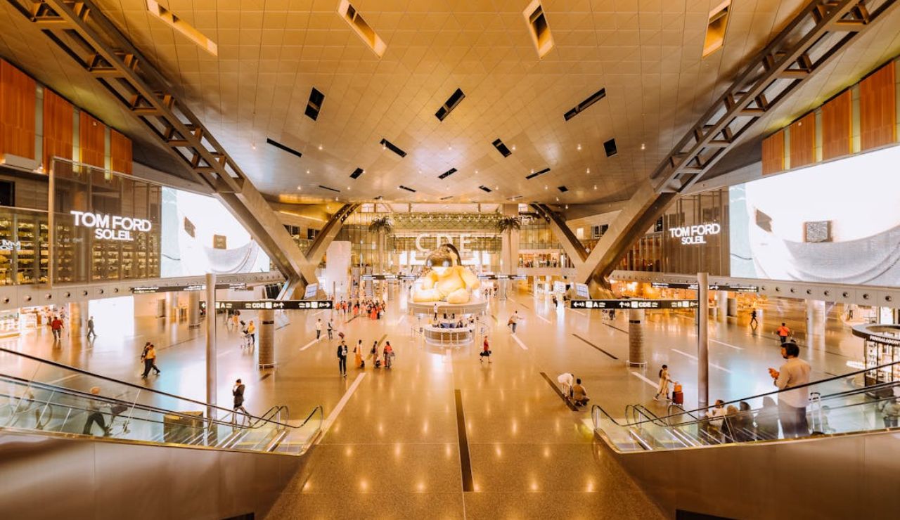 Spacious modern airport terminal with travelers and a large golden teddy bear sculpture.
