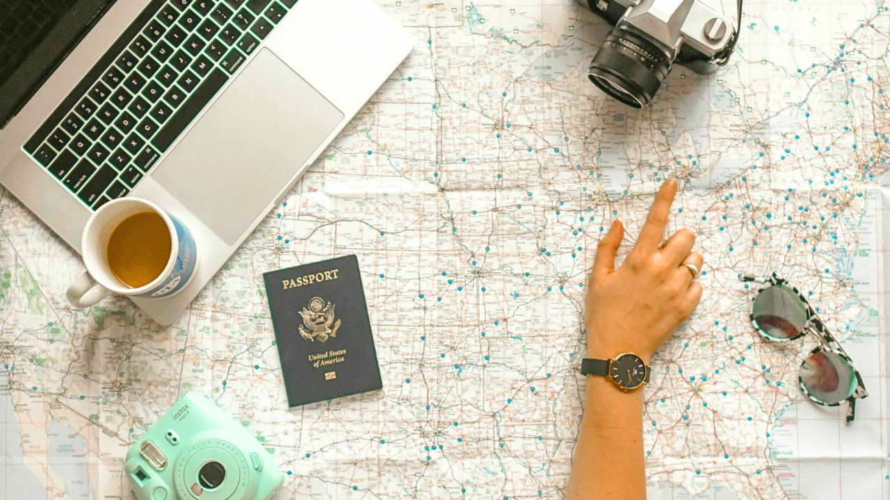A flat lay of travel essentials including a passport, boarding pass, travel journal, and laptop with map.