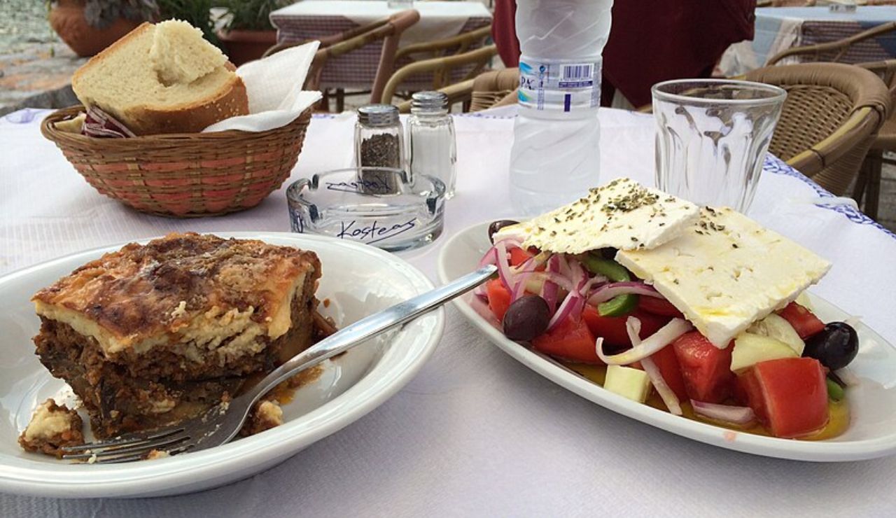 Traditional Greek meal with moussaka and a fresh Greek salad topped with feta cheese, served on an outdoor restaurant table.