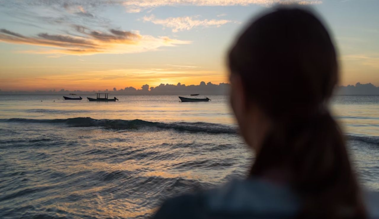 Girl watching boats on the calm ocean at sunrise from Tulum Beach, Mexico.