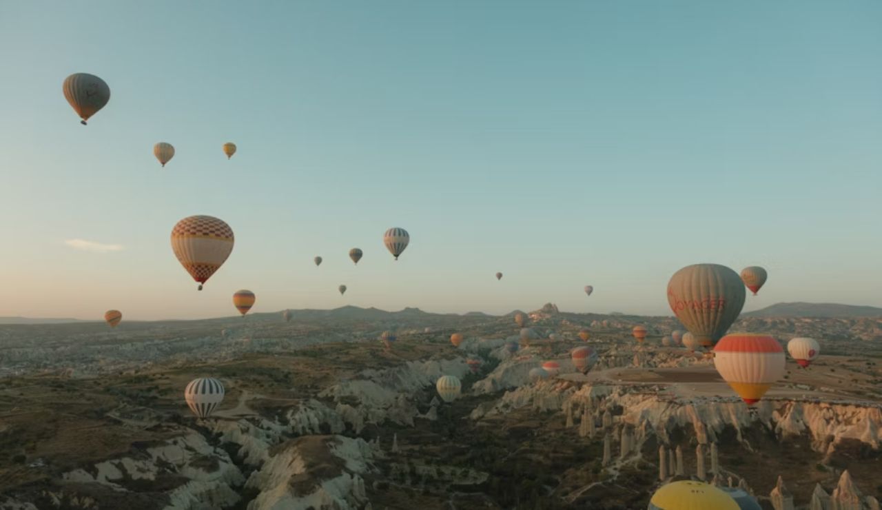 Hot air balloons floating over a rocky valley landscape during sunrise or sunset.