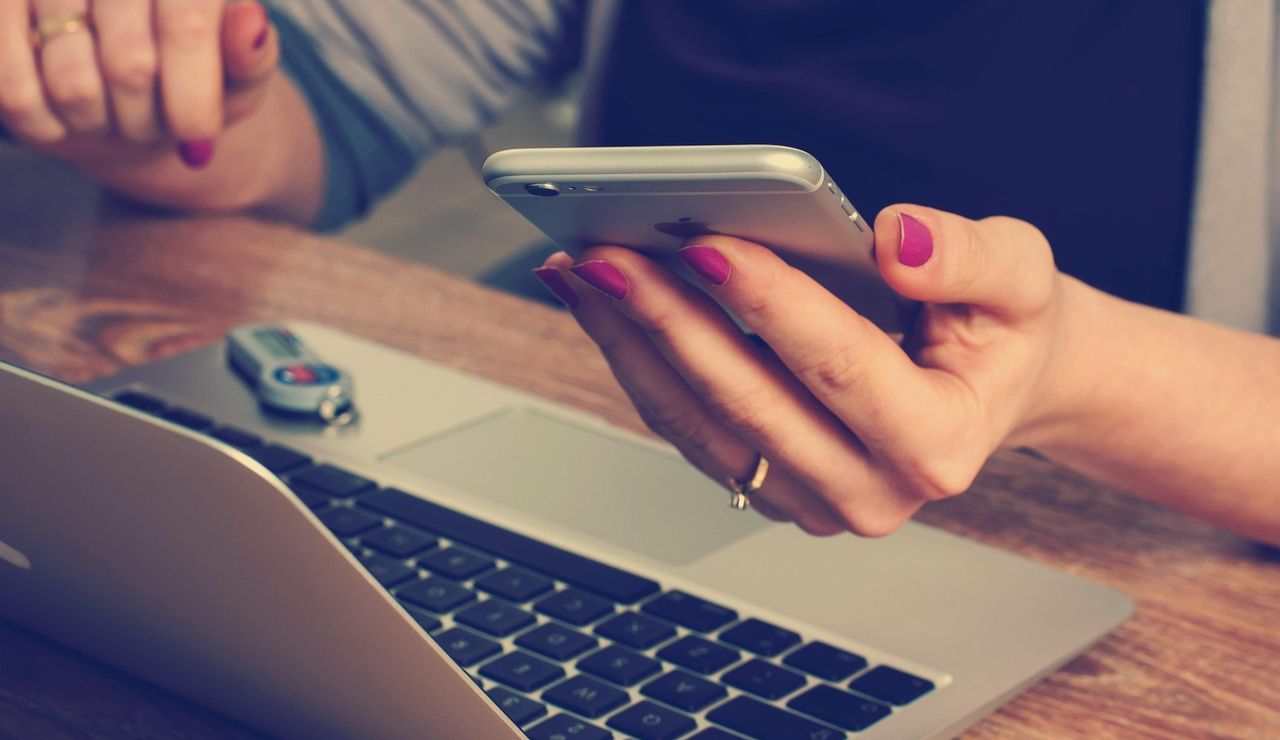 Person holding a smartphone while using a laptop, with a USB drive plugged in.