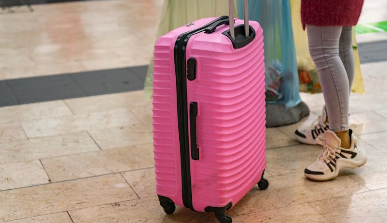 Bright pink hard-shell suitcase on wheels next to a person wearing sneakers and leggings in an indoor travel setting.