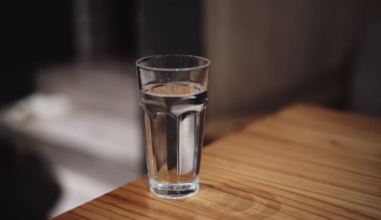 Clear glass of water placed on a wooden table in soft indoor lighting.